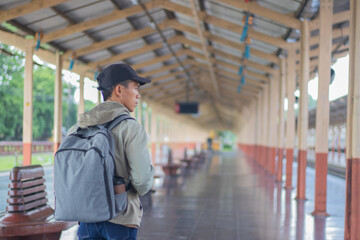 Confident young latin man standing alone at sunrise. Standing on train station platform, holding...