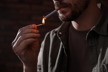 Man lighting cigarette with match on blurred background, closeup