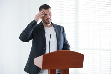 Fear of public speaking. Nervous man with microphone at lectern indoors