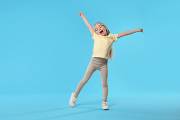 Obraz premium Cute little girl dancing on light blue background, space for text