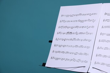 Note stand with music sheets on light blue background, closeup. Space for text