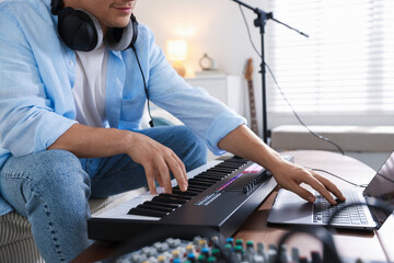 Man working with MIDI keyboard and laptop at table indoors, closeup