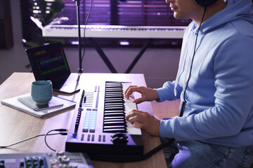 Man working with MIDI keyboard at table in home studio, closeup