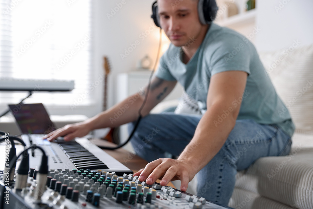 Poster man working with dj mixer and midi keyboard on sofa indoors, selective focus