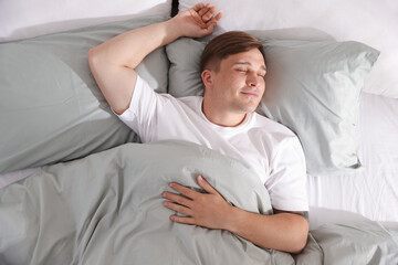 Young man sleeping on bed with soft mattress at home, top view