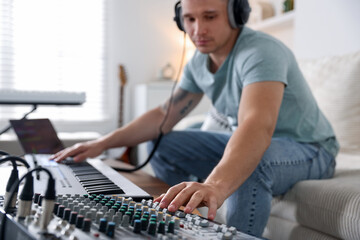 Man working with dj mixer and MIDI keyboard on sofa indoors, selective focus