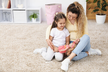 Mother and her daughter playing with doll on floor at home