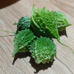 A pile of vibrant green bitter melons with bumpy textured skin resting on a wooden surface