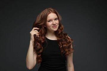 Fototapeta premium Portrait of beautiful teenage girl with healthy wavy hair on dark grey background