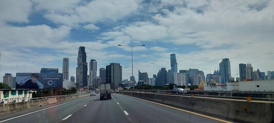 Busy highway approaching a modern city skyline with skyscrapers under a cloudy sky
