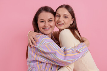 Two happy friends hugging on pink background