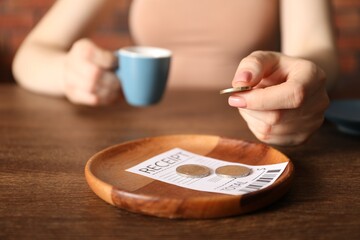 Woman putting tips onto plate at wooden table in cafe, closeup