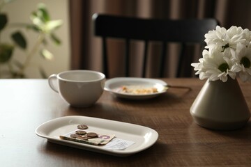 Tips, receipt, chrysanthemum flowers, dirty plate and cup on wooden table in cafe, closeup