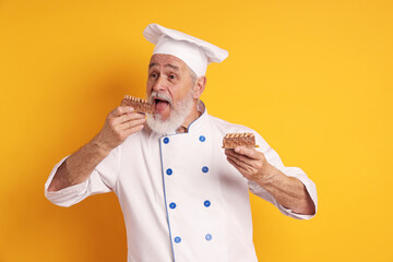 Professional pastry chef eating delicious dessert on orange background