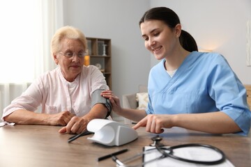 Fototapeta premium Nurse measuring patient's blood pressure at wooden table indoors. Home health care service