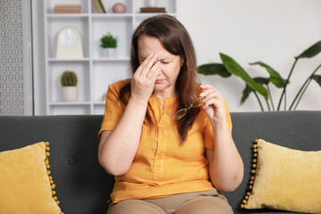 Woman with glasses suffering from eyestrain on sofa at home