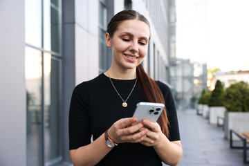 Successful businesswoman with smartphone near office building