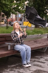 Woman with broken umbrella on bench outdoors