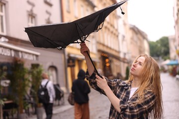 Woman with broken umbrella on city street