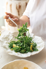 Woman eating green salad with avocado and arugula from white plate