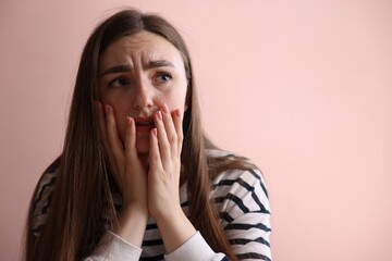 Scared woman suffering from paranoia near beige wall indoors, space for text