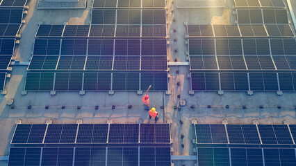 A bird's-eye view of two workers in orange vests inspecting a vast solar panel field, symbolizing...