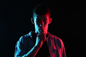 Man using electronic smoking device in neon lights on black background