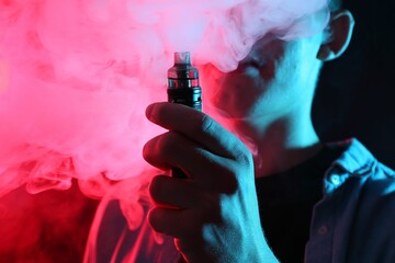 Man using electronic smoking device in neon lights on dark background, closeup