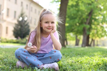 Cute little girl with beautiful dandelion on grass outdoors