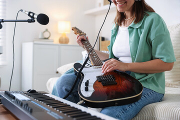 Smiling woman working with MIDI keyboard and guitar at table in home studio, closeup