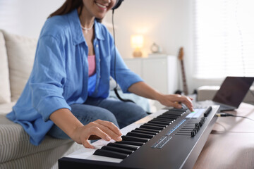 Smiling woman working with MIDI keyboard at table in home studio, closeup
