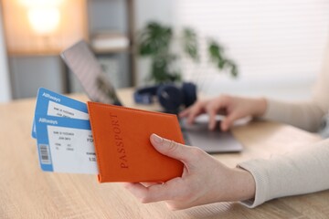 Woman with passport and flight tickets using laptop at wooden table indoors, closeup