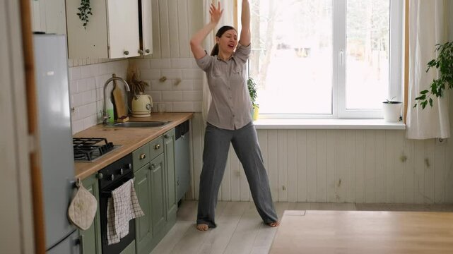 Brunette woman dance, have fun at home listens song, moves to music, feels overjoyed, celebrate good news, relish carefree life looks happy. Young adult female twirls, grooves. Lady dancing in kitchen