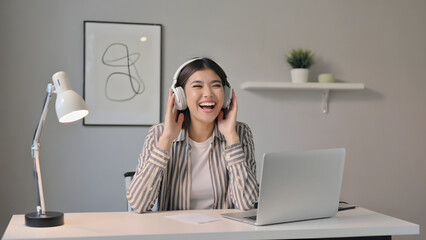 Happy woman in striped shirt enjoying video call with headphones at home office