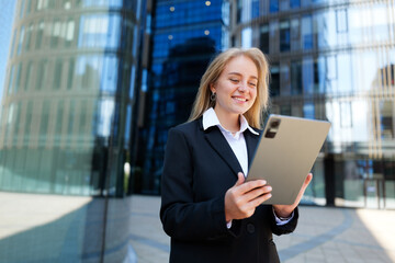 Business professional smiles while using a tablet outside a modern office building in the early afternoon