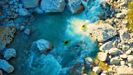 Two kayakers tackle turquoise river rapids, skillfully navigating jagged rocks. Drone shot captures the thrill and raw power of nature's adventure.