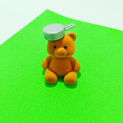 Close-up of a brown teddy bear sitting on a vivid green surface, playfully balancing a small gray...