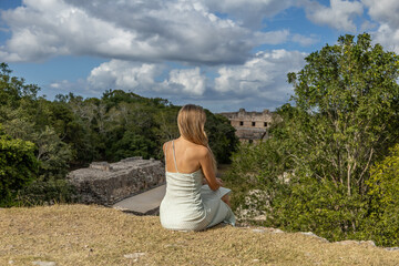 Woman with long blonde hair is sitting and enjoying the view at the majestic Mayan ruins of Uxmal...