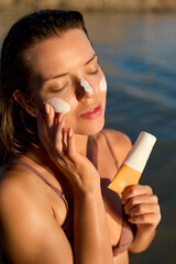 Suntan lotion. Woman applying sunscreen solar cream on face. Beautiful happy cute girl puts suntan...