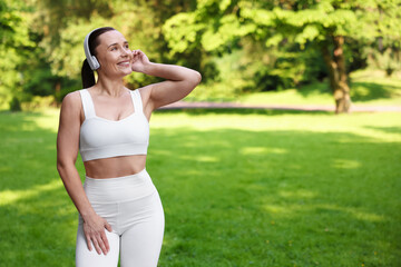 Woman in sportswear and headphones in park, space for text