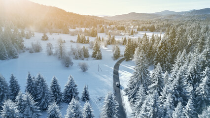 An aerial view of a winding mountain road showcases a car driving through a snowy forest. The scene highlights the thrill of alpine driving and winter travel adventures.