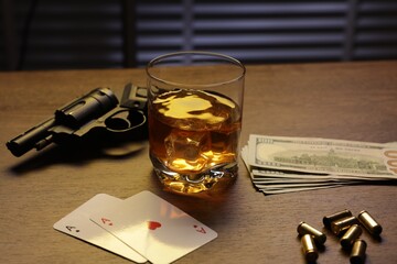 Mafia and criminal world. Gun, bullets, money, whiskey and playing cards on wooden table, closeup