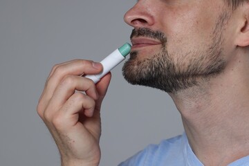 Man applying lip balm onto his lips on grey background, closeup