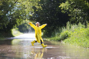 Happy An eight-year-old girl wearing yellow rubber boots and a yellow raincoat Jumping in a puddle...