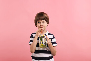 Cute little boy drinking lemonade on pink background. Refreshing drink