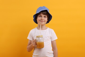 Cute little boy in panama hat with mason jar of juice on orange background. Refreshing drink