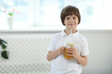 Cute little boy with mason jar of orange juice at home, space for text. Refreshing drink