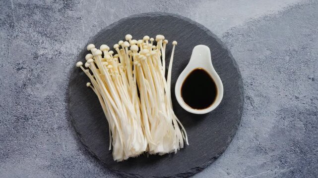 Fresh enoki mushrooms with soy sauce on round slate plate

