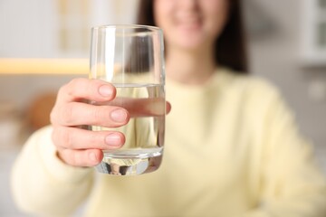 Woman drinking water from glass in kitchen, selective focus