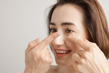 Woman putting in contact lens on light background, closeup